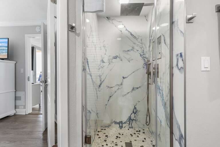 Elegant shower with marble-patterned walls and pebble flooring, offering a spa-like experience.