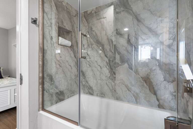 Luxurious shower with marble-patterned walls and a sleek glass enclosure.