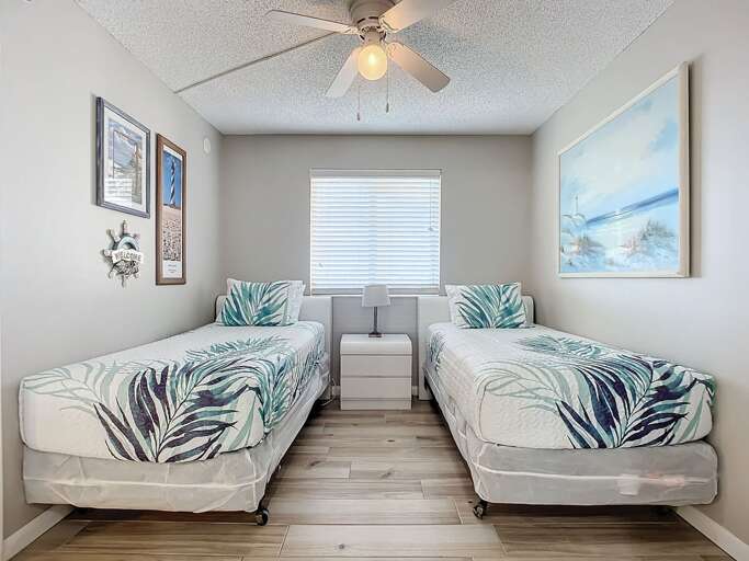 Bright and airy room featuring twin beds with tropical bedding, coastal artwork, and a calming ambiance for a restful stay.
