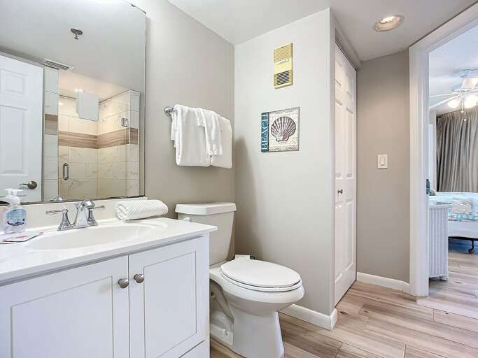 Bright bathroom featuring a modern vanity, large mirror, and beach-inspired accents. Conveniently located next to the bedroom for added comfort.