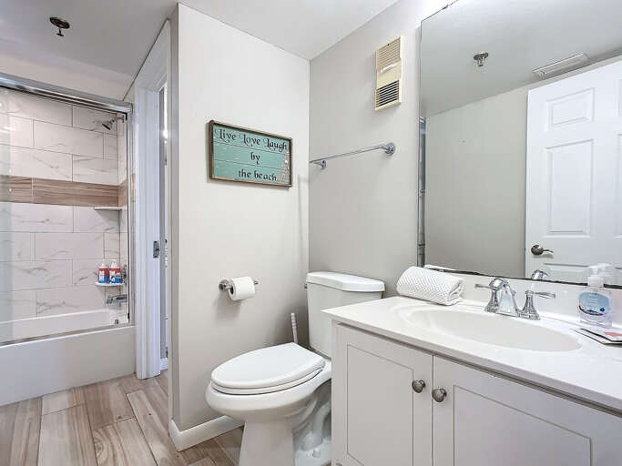 Clean and bright bathroom featuring a tub-shower combo, stylish tiles, and beach-themed decor for a refreshing and relaxing space.