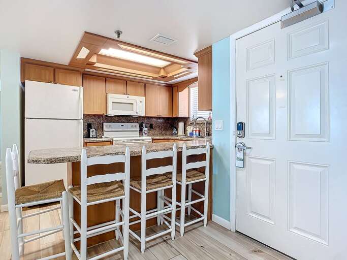Fully equipped kitchen featuring granite counters, wood cabinetry, and a breakfast bar with seating for four. Ideal for cooking and gathering.