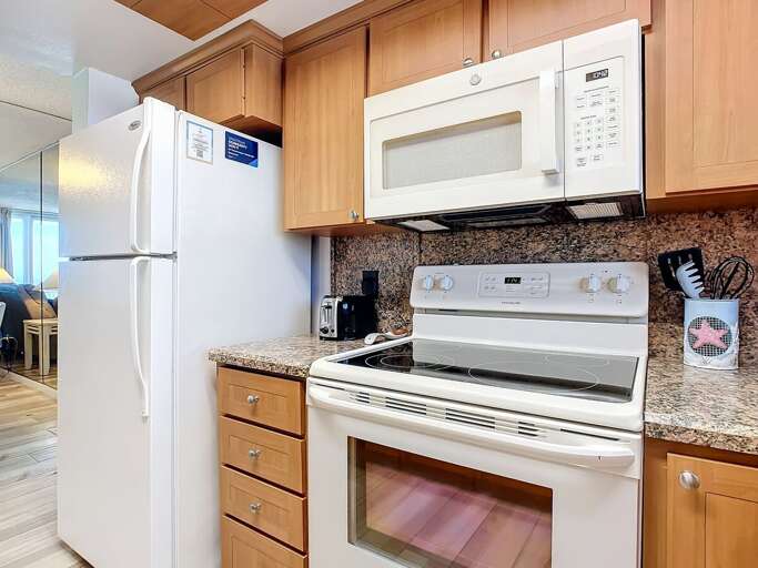 Functional kitchen includes a refrigerator, microwave, and stove, complemented by granite countertops and ample storage for a comfortable cooking experience.