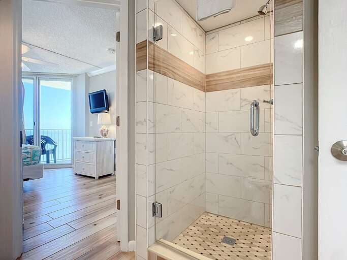 Stylish walk-in shower featuring marble-inspired tiles, wood accents, and modern fixtures. A perfect complement to the serene bedroom nearby.