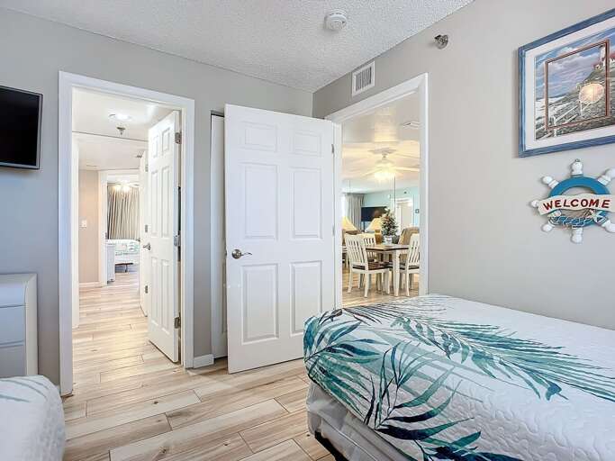 Twin bedroom offering tropical decor, a wall-mounted TV, and easy access to the living and dining areas for a seamless, welcoming experience.