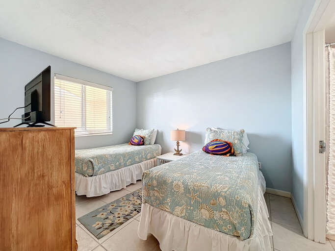 This charming twin bedroom features nautical-themed bedding, a flat-screen TV, and ample natural light, creating a relaxing retreat for guests.