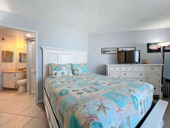 Retreat to this coastal-themed bedroom featuring a comfortable bed, ample storage, a flat-screen TV, and an en-suite bathroom for added convenience.
