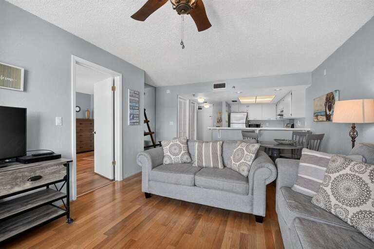 Enjoy an inviting open-concept living area with comfortable seating, TV, dining space, and easy access to the kitchen—perfect for gathering and unwinding together after a memorable day at the beach.