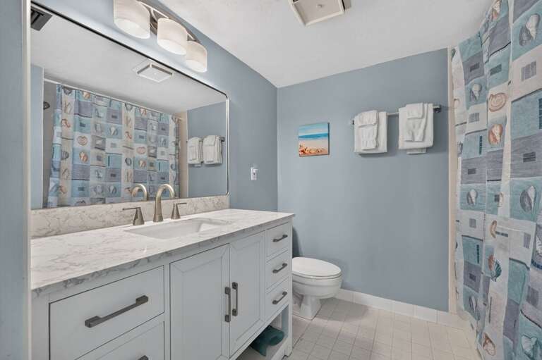 Freshen up in this bright coastal bathroom featuring a spacious vanity, large mirror, and beach-inspired accents. A clean and convenient space designed for comfort during your relaxing beach stay.