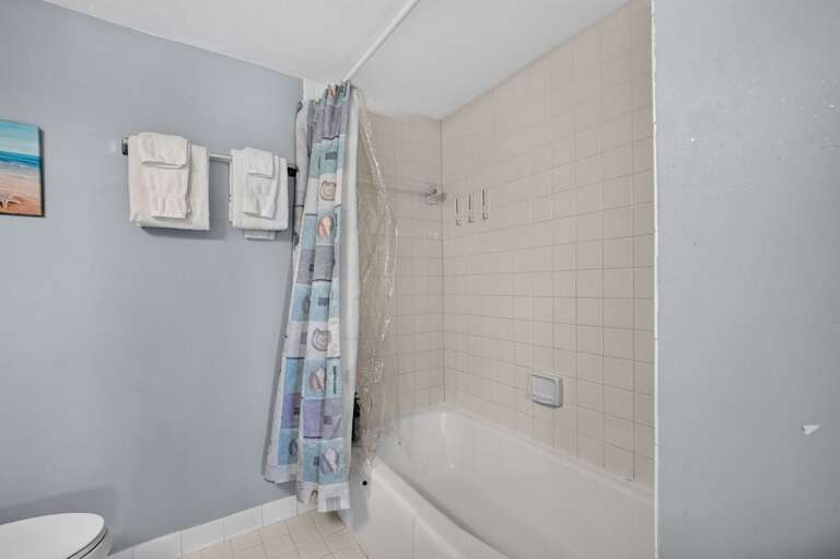 Refresh after a day at the beach in this convenient bathroom featuring a tub and shower combination, fresh towels, and coastal-inspired accents—a practical addition to your comfortable beach stay.