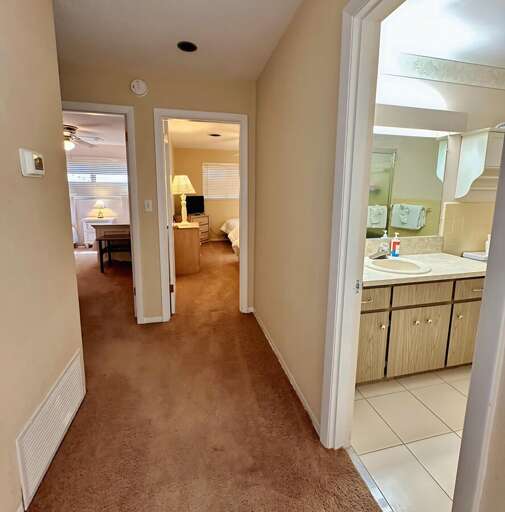 Central hallway leads to multiple cozy bedrooms and a convenient full bathroom with a wide vanity, plenty of mirror space, and fresh towels provided.