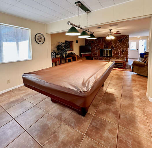 Enjoy a game night in this bright, tiled room featuring a full-size pool table under classic green billiard lights! Just off the cozy living area with a stone fireplace and comfy seating.