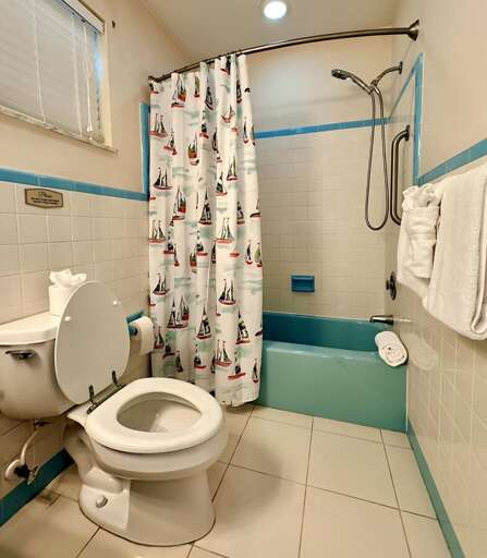 Fun and functional bathroom featuring a retro-style aqua bathtub, nautical shower curtain, and a combo tub/shower with handheld sprayer. Stocked with fresh towels, toiletries, and bright lighting.