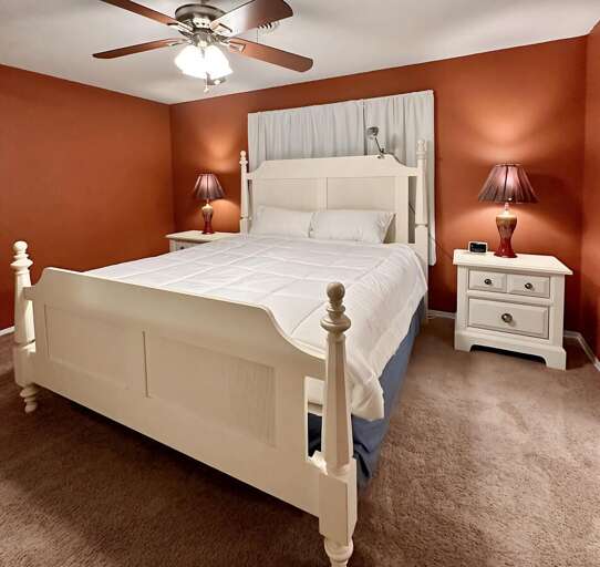 Spacious and cozy bedroom featuring a plush king-size bed with crisp white linens, warm accent lighting, and matching nightstands.
