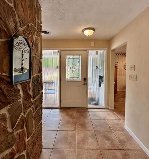 Step into a warm and welcoming entryway featuring a decorative glass front door, tiled flooring, and