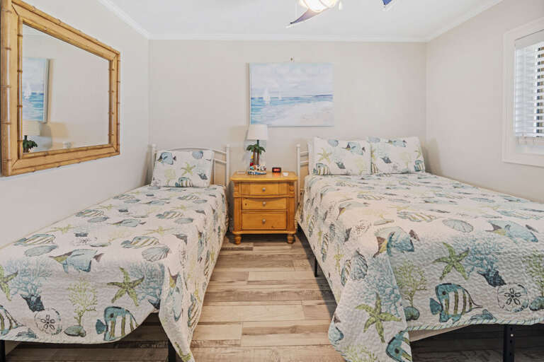 Perfect for family beach stays, this bright bedroom offers a twin and full bed with ocean-themed bedding, light wood furnishings, and seaside décor for a cheerful coastal retreat.