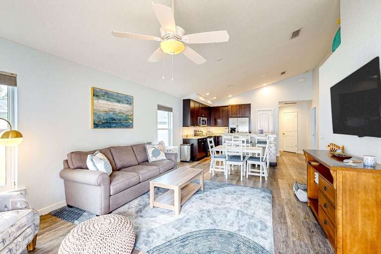 Bright open-concept living and dining area with beachy décor, cozy seating, and easy flow to the kitchen—perfect for relaxing after sun-filled days on the coast.