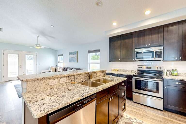 Bright, beach-style kitchen with granite counters and stainless appliances, opening to a cozy living space—perfect for gathering after sun-soaked coastal adventures.