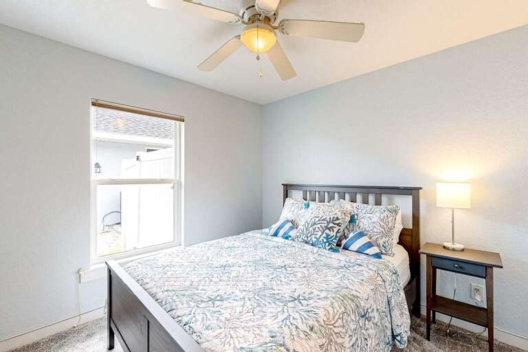 Calming beach-inspired bedroom featuring soft coastal bedding, warm lighting, and a bright window—an inviting retreat after a day of sun, sand, and seaside fun.