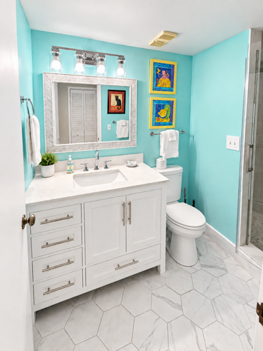 The primary bathroom features a spacious vanity with ample storage, a walk-in glass-enclosed shower, and bright coastal décor.