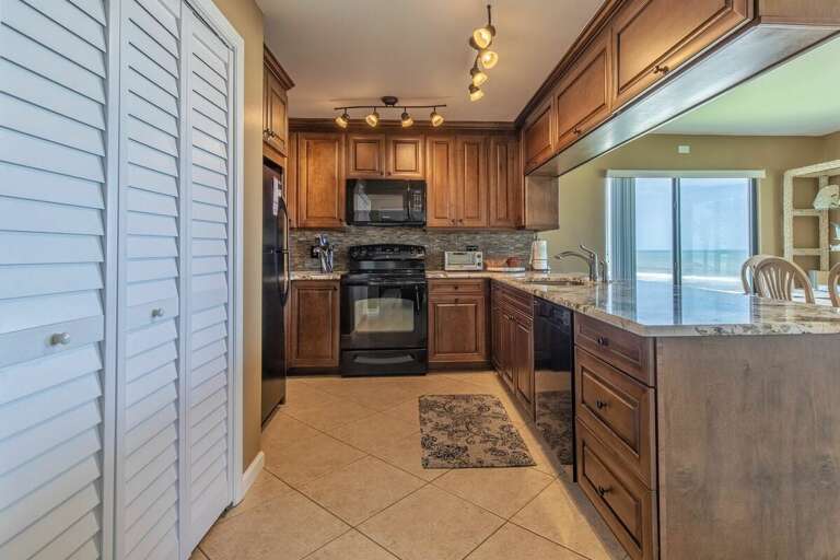 Cook with a view in this fully equipped beachfront kitchen featuring granite countertops, warm cabinetry, and ocean views—perfect for preparing meals during your relaxing beach stay.