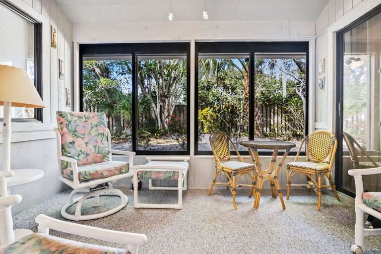 Bright sunroom with large windows, cozy seating, and garden views—perfect for morning coffee or evening relaxation. This charming beach stay space blends indoor comfort with a breezy coastal feel.