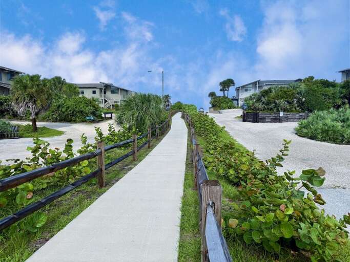 Peaceful walkway lined with lush coastal greenery leading toward the ocean. This charming beach stay setting offers easy access to sun, sand, and sea for the ultimate seaside getaway.