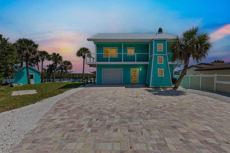 Bright beach house getaway with tropical palms, large driveway, and elevated design. Perfect for a