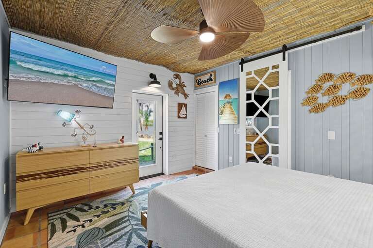 Relax in this bright coastal bedroom featuring a woven ceiling, beach-inspired art, and private