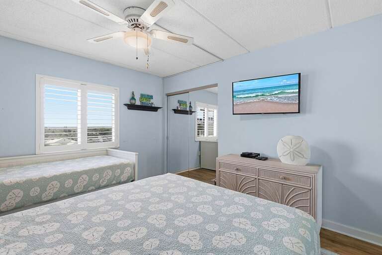 Relax in this bright beach stay bedroom featuring cozy bedding, coastal décor, and a TV for added comfort. A peaceful space to unwind after enjoying sun-filled days by the beach.