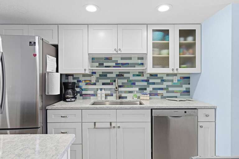 This beach stay features a sleek coastal kitchen with modern appliances, bright cabinetry, and a colorful tile backsplash. A perfect space to cook, relax, and enjoy your seaside getaway.