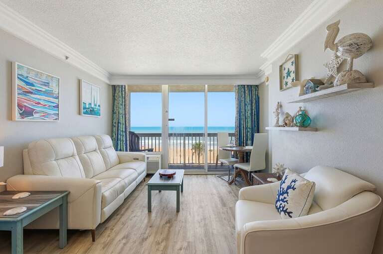 Bright and inviting beach stay living space with ocean views, cozy seating, and direct access to a private balcony. Relax indoors or step outside to enjoy the coastal breeze just steps from the sand.