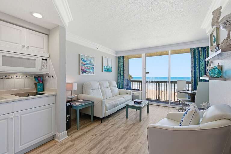 Open-concept beach stay with cozy seating, kitchenette, and dining area leading to a private balcony with ocean views. Enjoy a relaxing coastal retreat just steps from the sand and surf.