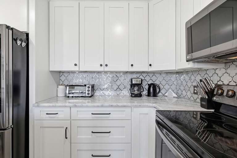 This beach stay kitchen features clean white cabinetry, modern appliances, and stylish backsplash