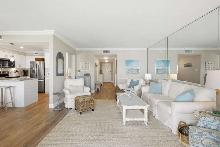 Enjoy a stylish beach stay in this bright coastal condo featuring an open living area, comfortable seating, mirrored accents, and a modern kitchen perfect for relaxing vacations by the shore.