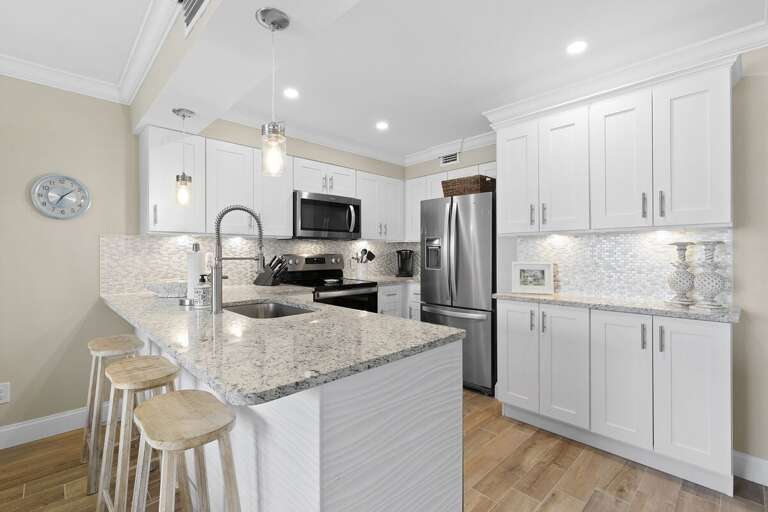 This stylish beach stay kitchen features granite countertops, stainless steel appliances, custom cabinetry, and bar seating—perfect for preparing meals and gathering after a day by the ocean.