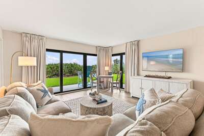 Relax in this bright coastal living room with comfortable seating, large windows, and direct patio