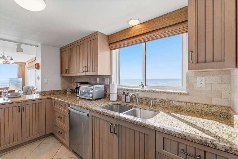 Prepare your favorite meals with an ocean view in this inviting kitchen, featuring granite countertops, ample cabinetry, and modern appliances—a convenient and scenic space for your beach stay.