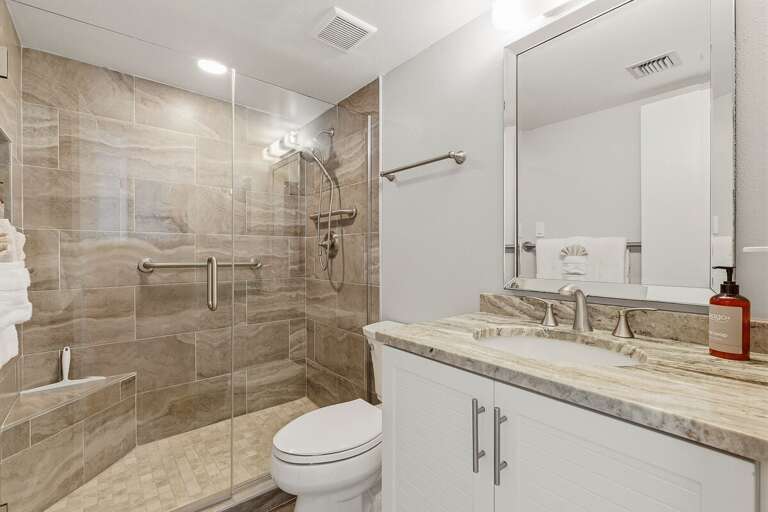 Refresh after a day at the beach in this bright bathroom featuring a spacious glass-enclosed walk-in shower, modern vanity, and convenient grab bars for added comfort during your beach stay.