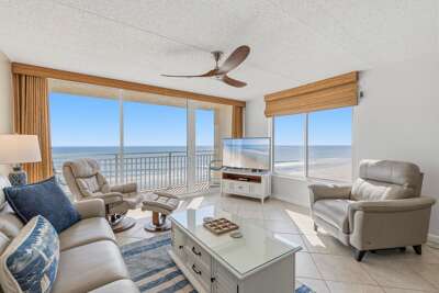 Relax in a bright, comfortable oceanfront living room featuring floor-to-ceiling windows, coastal décor, and sweeping Atlantic views—an inviting space to unwind and enjoy your beach stay.