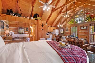 Spacious open-concept cabin — cozy living, dining, and sleeping spaces under soaring wood beams.