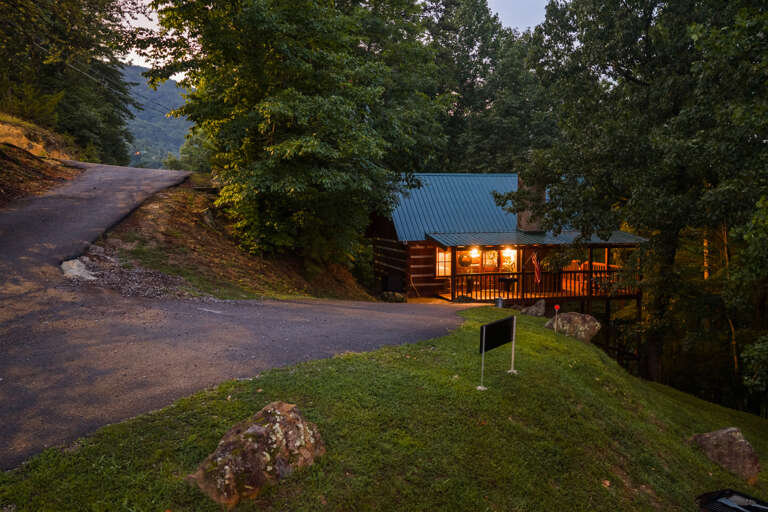 Follow the quiet mountain road home to Nestled Oaks, glowing warmly at dusk on private, wooded Bluff Mountain.