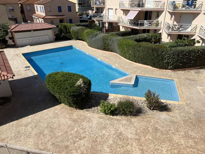 Sunlit Swimming Pool Surrounded By Shrubs And Buildings