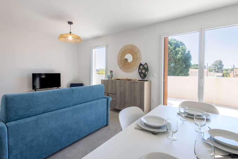 Bright Living Room With Blue Sofa, Sunlit Dining Area, And Balcony View