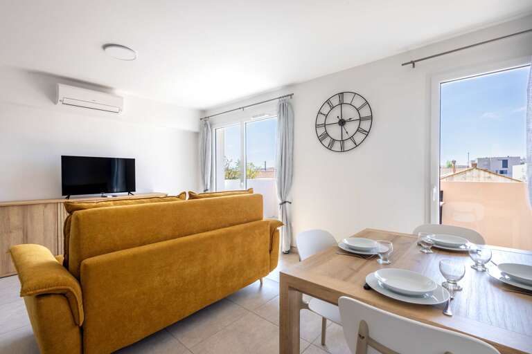 Sunlit Living Area With Mustard Sofa, Dining Table, And Wall Clock