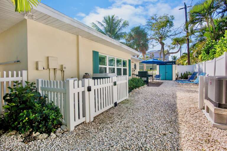 Charming tropical property exterior with white picket fence and palm tree landscaping in a peaceful residential setting.