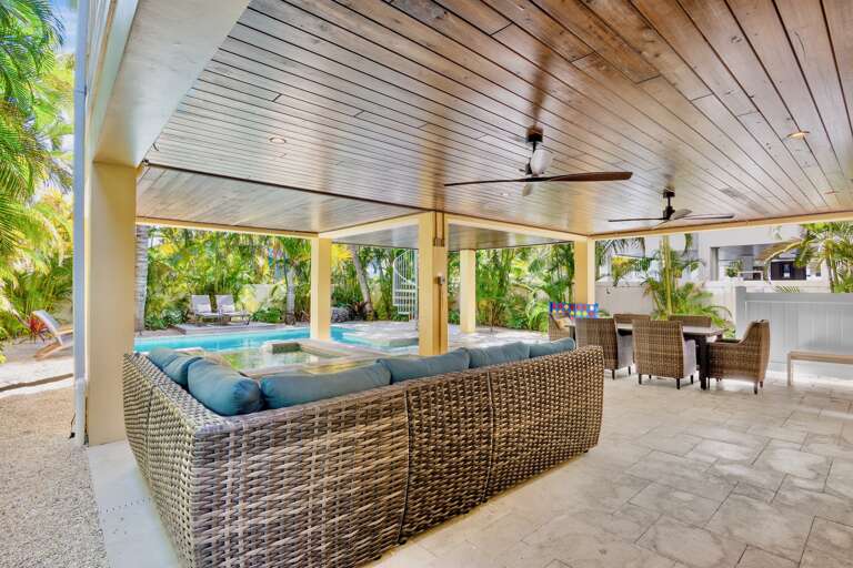 Your tropical oasis awaits with elegant covered living, where plush seating faces the sparkling pool amid swaying palms.
