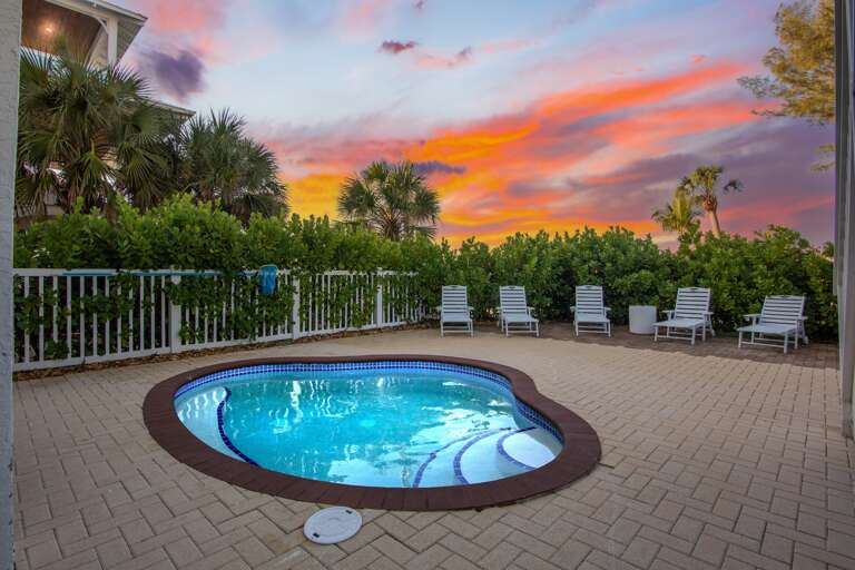 Stunning sunset paints the sky while tropical palms frame this private pool oasis with comfortable lounge chairs.