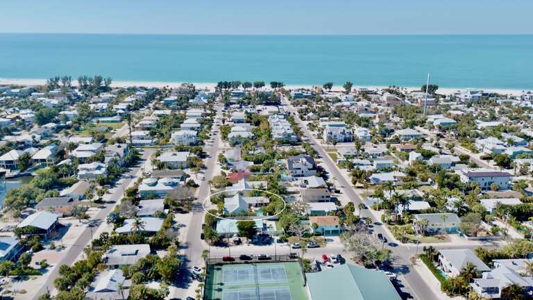 Aerial view of a charming beachside neighborhood with tree-lined streets leading to pristine white sand beaches and turquoise waters.
