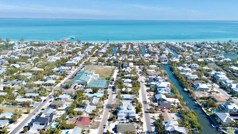 Aerial view of a tropical waterfront community with canal-front homes and pristine turquoise waters stretching to the horizon.